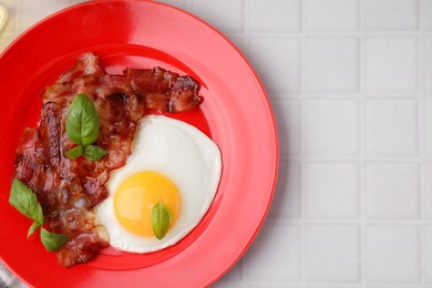 Photo of Fried egg, bacon and basil on white tiled table, top view. Space for text