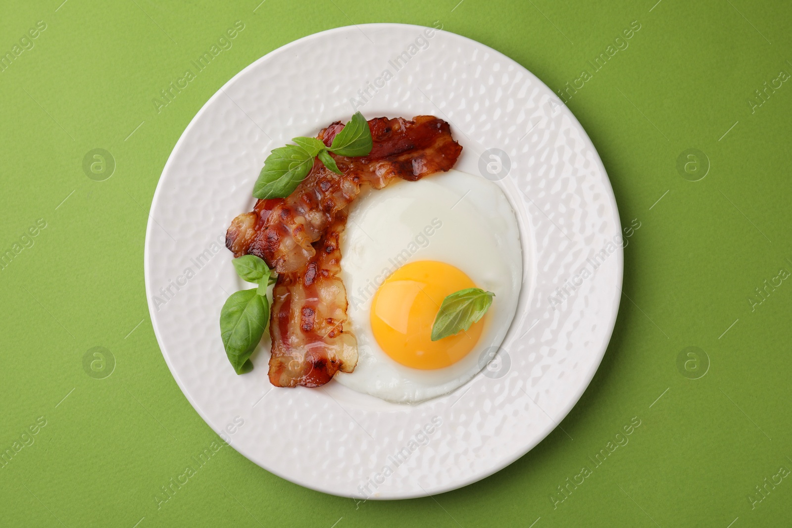 Photo of Fried egg, bacon and basil on green background, top view