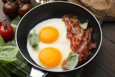 Fried eggs, bacon and basil in frying pan on wooden table