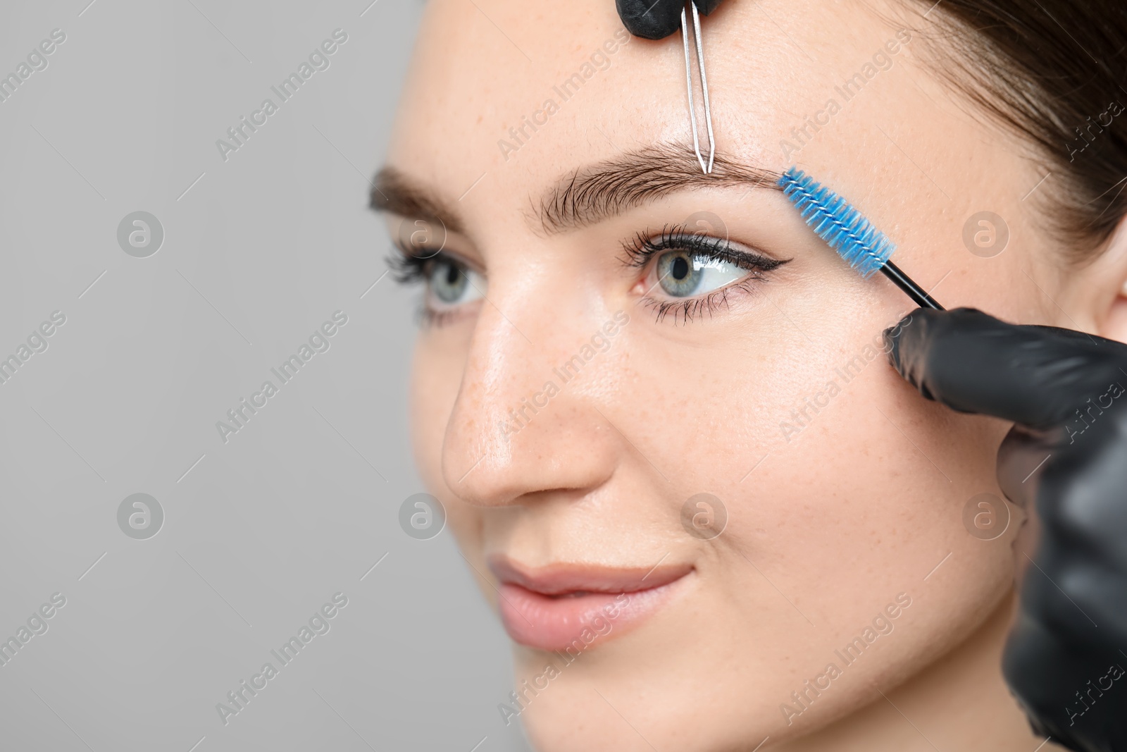 Photo of Beautician making eyebrow correction to young woman on light background, closeup. Space for text