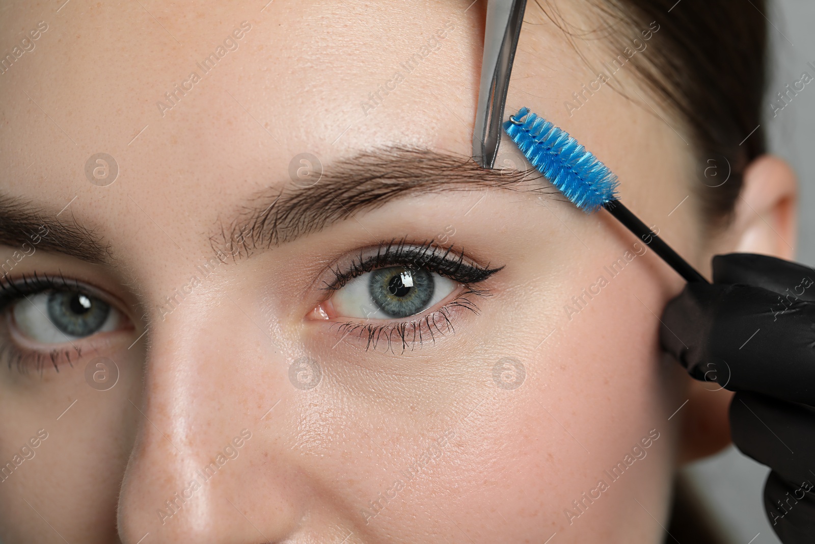 Photo of Beautician making eyebrow correction to young woman in beauty salon, closeup