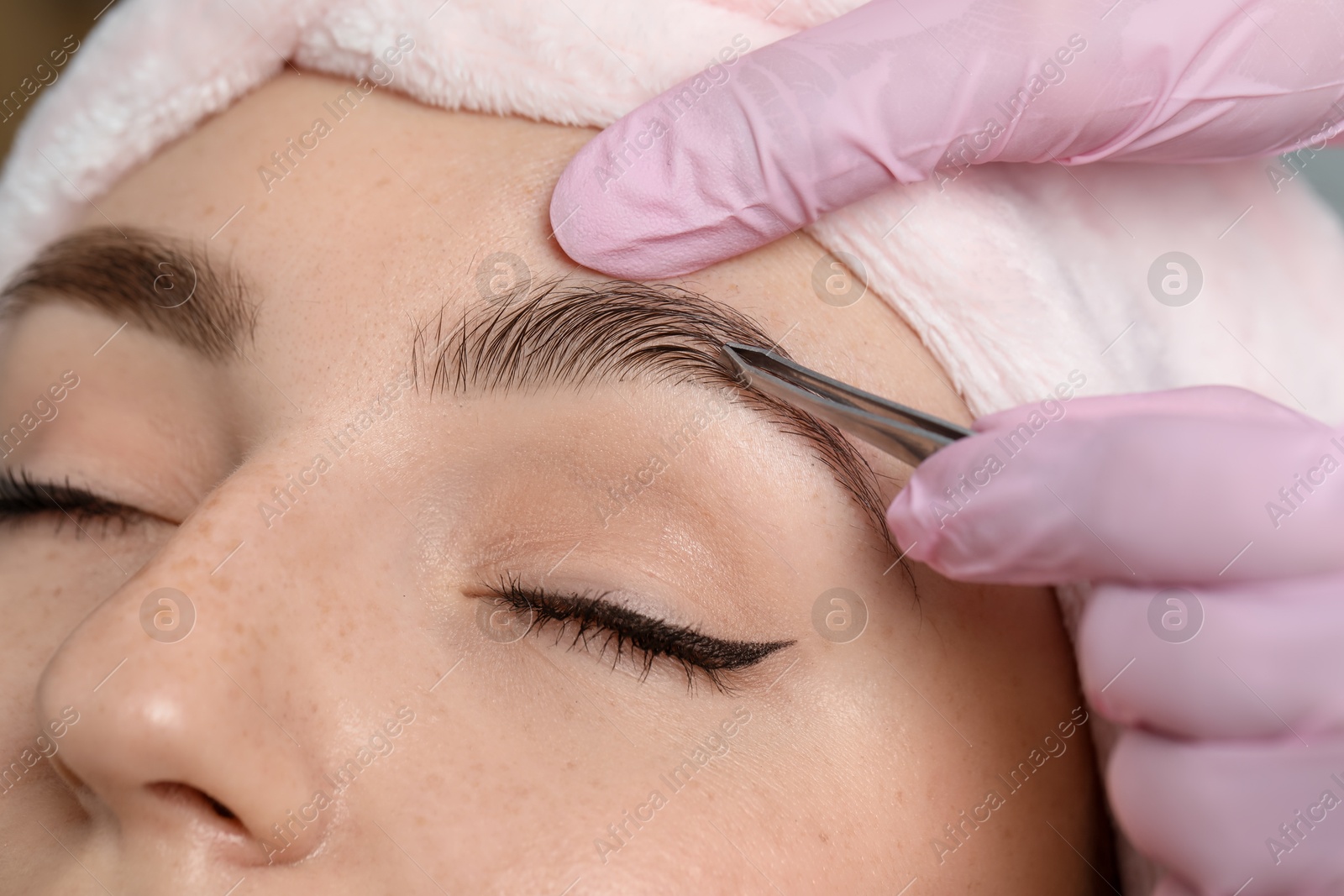 Photo of Beautician plucking young woman's eyebrow, closeup view