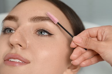 Photo of Beautician brushing young woman's eyebrow in beauty salon, closeup