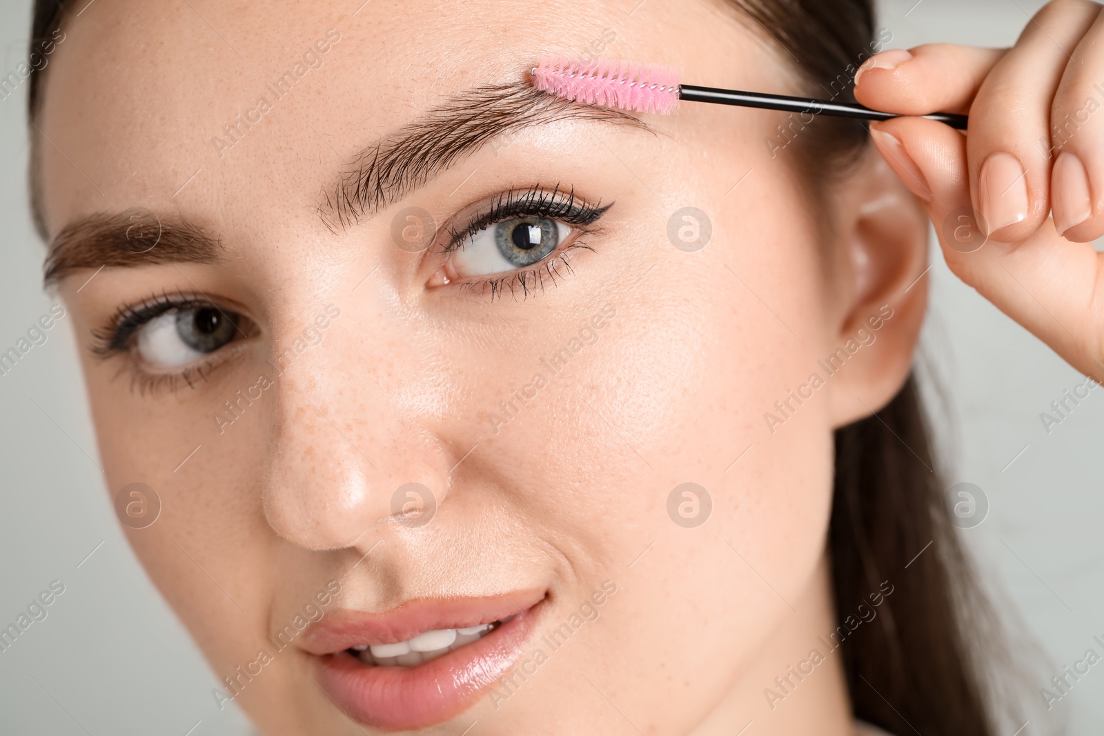 Photo of Young woman with spoolie brush on light background, closeup. Eyebrow correction