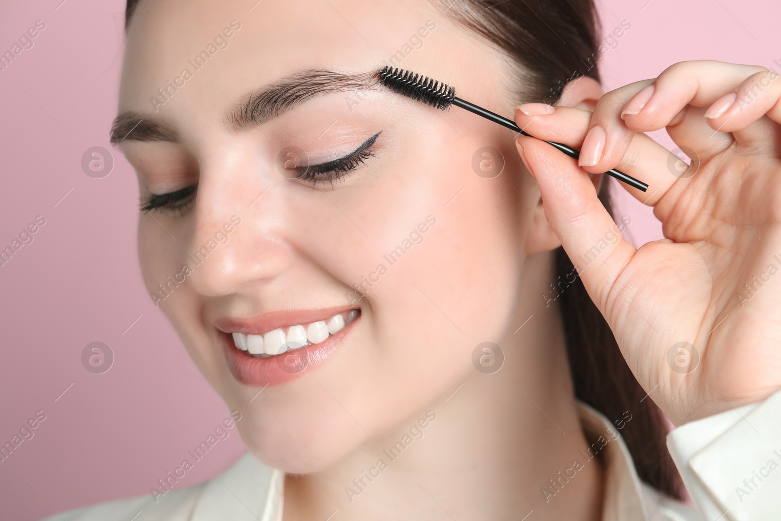 Photo of Young woman brushing eyebrow on pink background, closeup