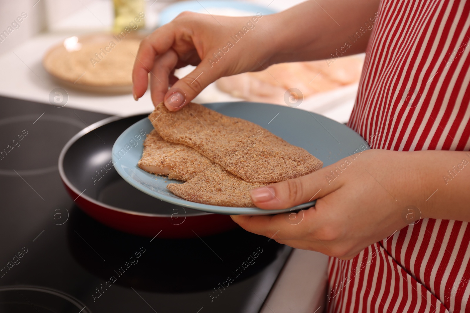 Photo of Woman holding raw schnitzels with breadcrumbs in kitchen, closeup