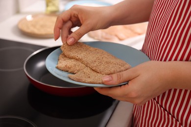 Photo of Woman holding raw schnitzels with breadcrumbs in kitchen, closeup