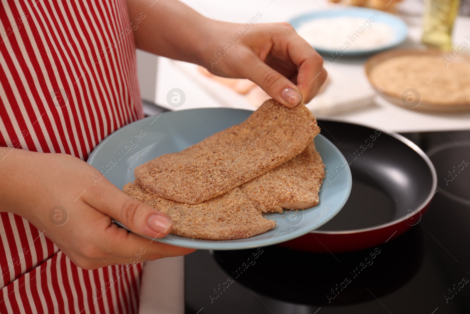 Photo of Woman holding raw schnitzels with breadcrumbs in kitchen, closeup