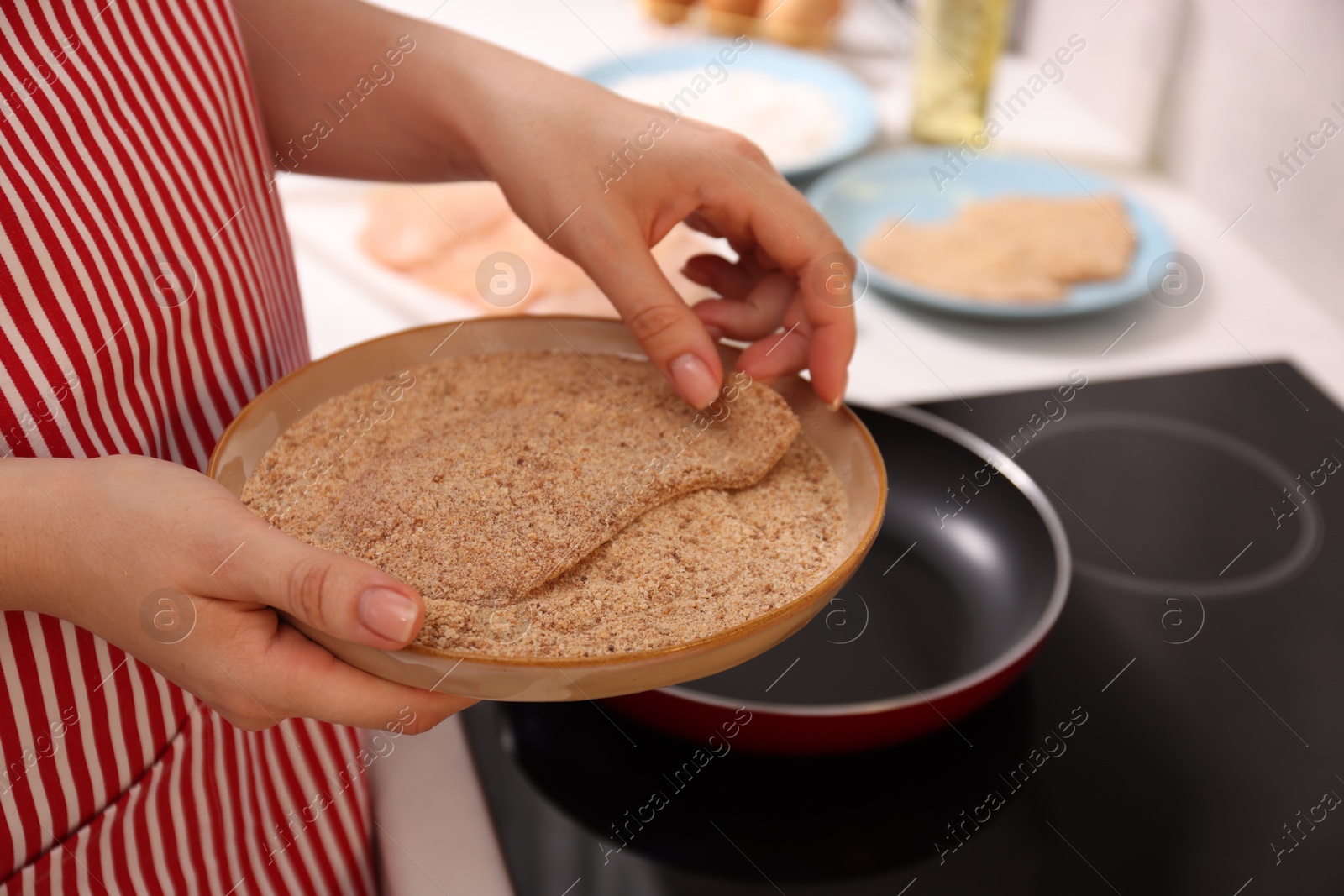 Photo of Woman holding raw schnitzels with breadcrumbs in kitchen, closeup