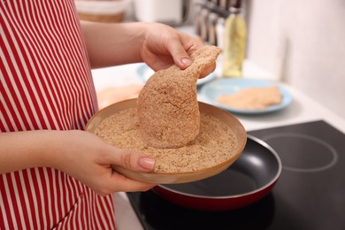 Woman holding raw schnitzels with breadcrumbs in kitchen, closeup