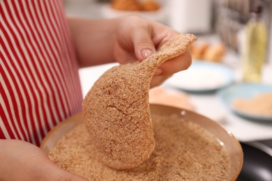 Photo of Woman holding raw schnitzels with breadcrumbs in kitchen, closeup