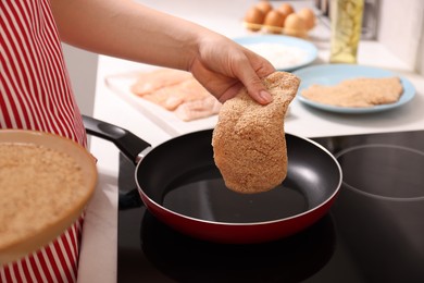 Woman cooking schnitzel in frying pan on stove, closeup