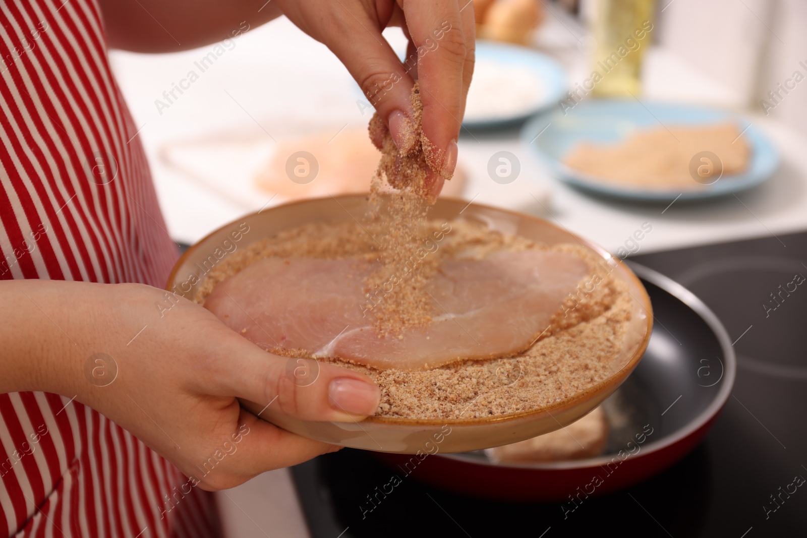 Photo of Woman holding raw schnitzels with breadcrumbs in kitchen, closeup