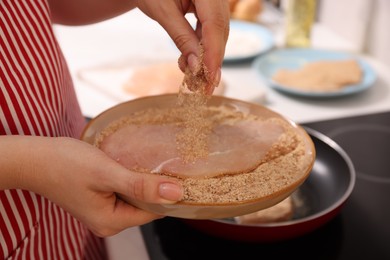 Woman holding raw schnitzels with breadcrumbs in kitchen, closeup