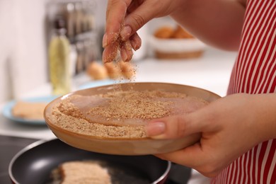 Photo of Woman holding raw schnitzels with breadcrumbs in kitchen, closeup