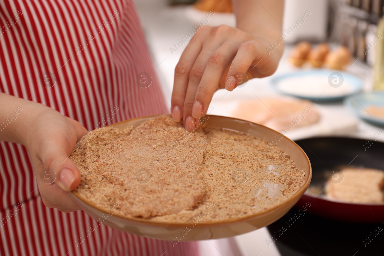 Photo of Woman holding raw schnitzels with breadcrumbs in kitchen, closeup