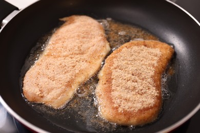 Photo of Schnitzels cooking in frying pan on stove, closeup