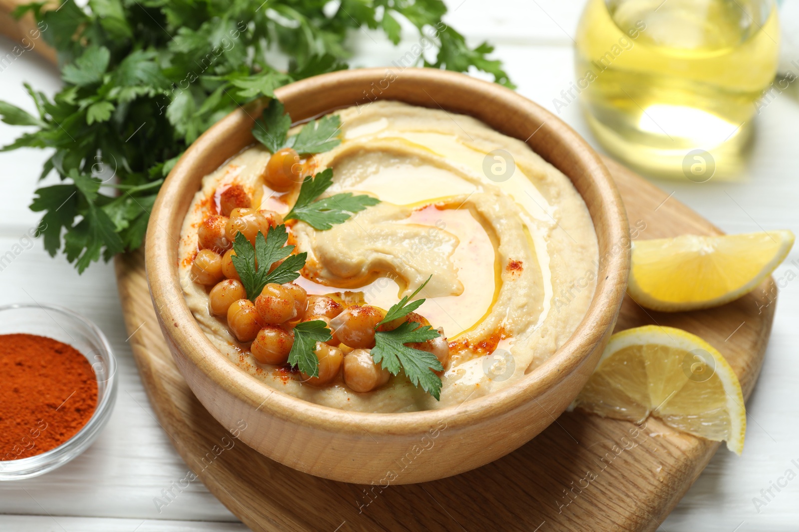 Photo of Delicious hummus with olive oil, chickpeas and parsley served on white wooden table, closeup