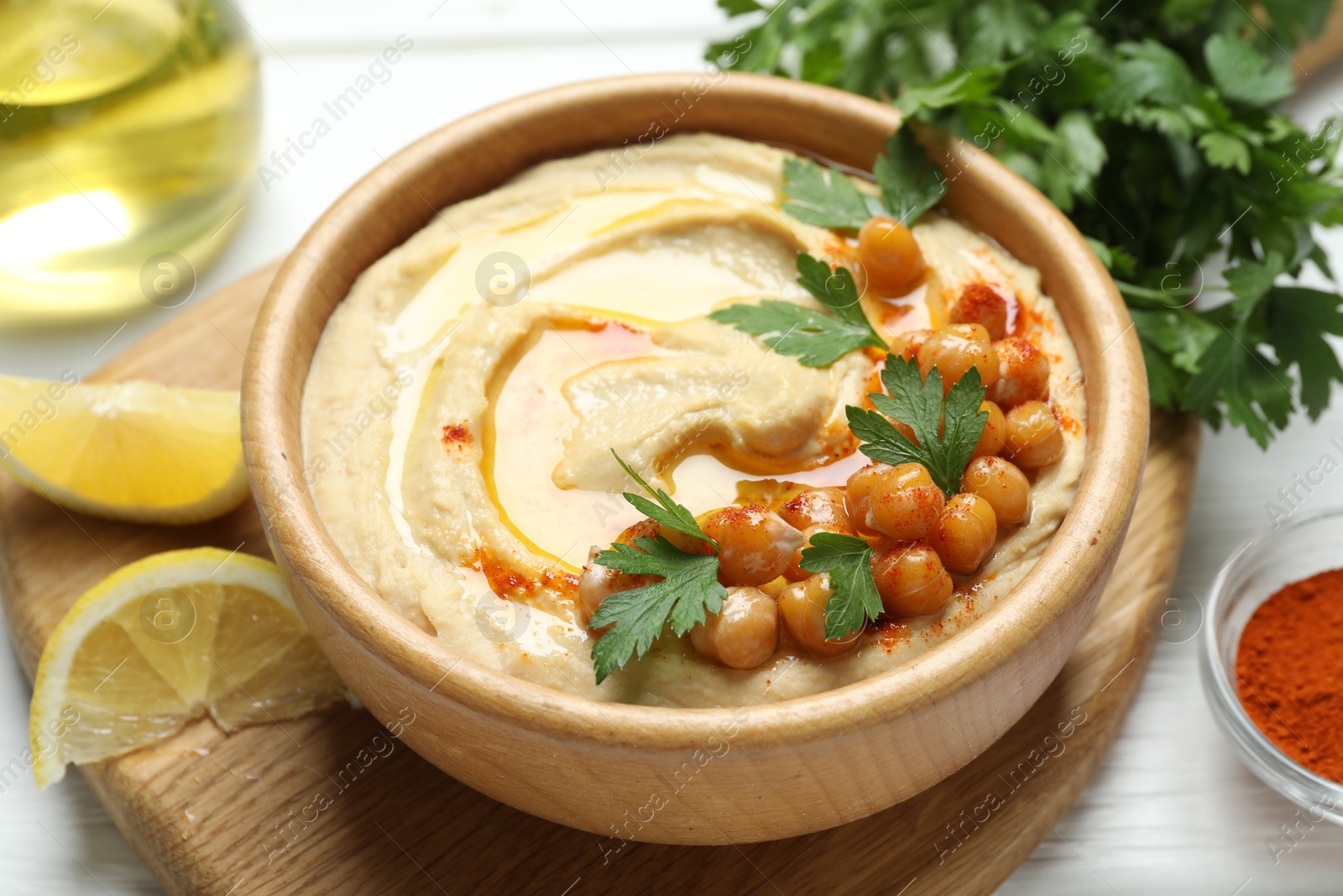 Photo of Delicious hummus with olive oil, chickpeas and parsley served on white wooden table, closeup