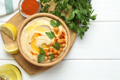 Delicious hummus with olive oil, chickpeas and parsley served on white wooden table, flat lay