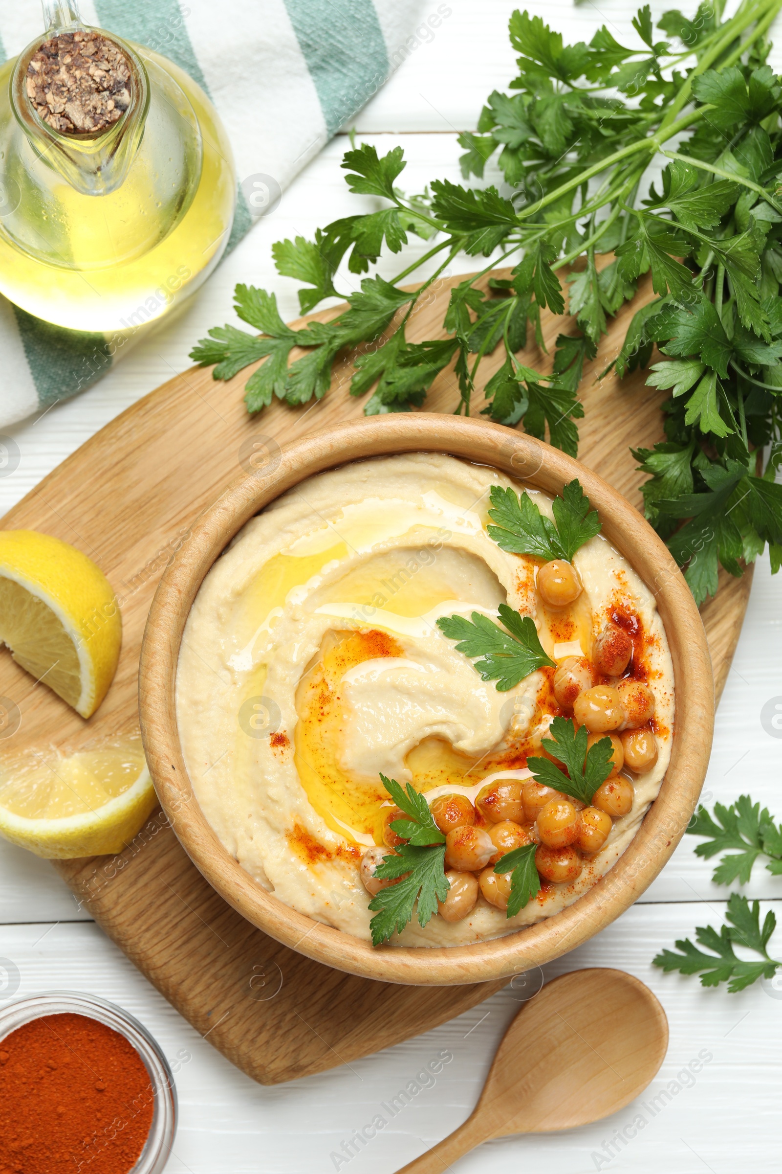 Photo of Delicious hummus with olive oil, chickpeas and parsley served on white wooden table, flat lay