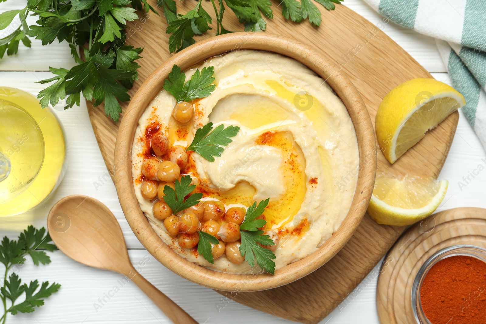 Photo of Delicious hummus with olive oil, chickpeas and parsley served on white wooden table, flat lay