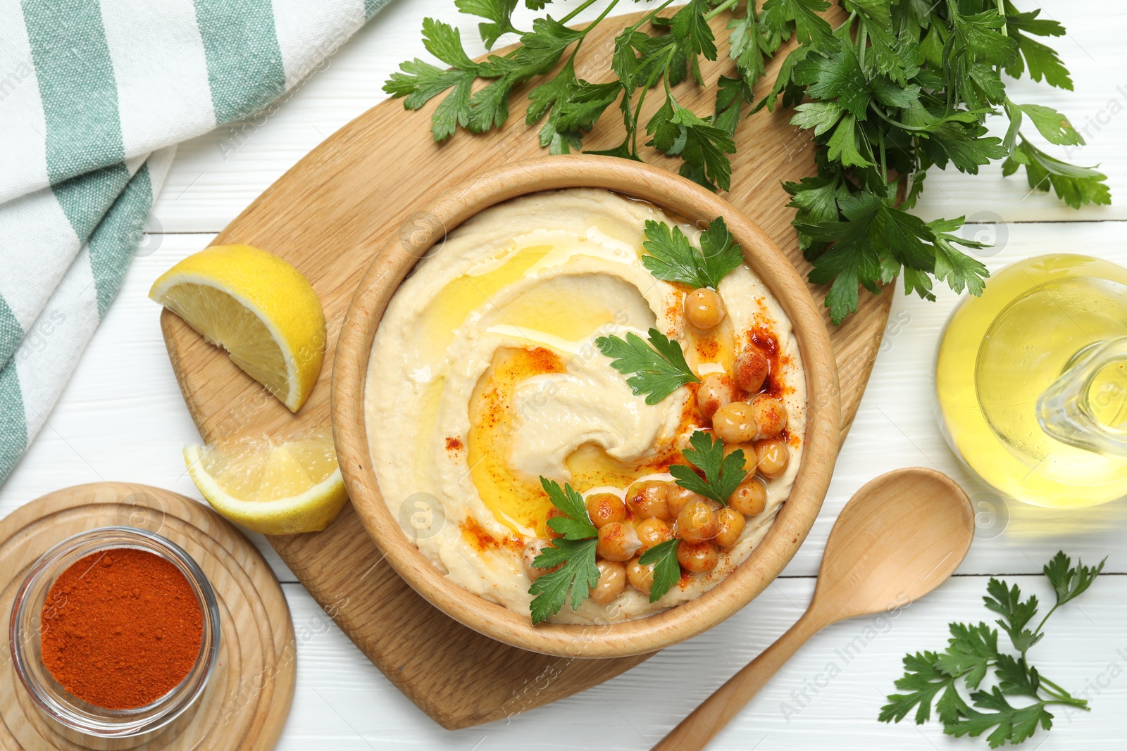 Photo of Delicious hummus with olive oil, chickpeas and parsley served on white wooden table, flat lay