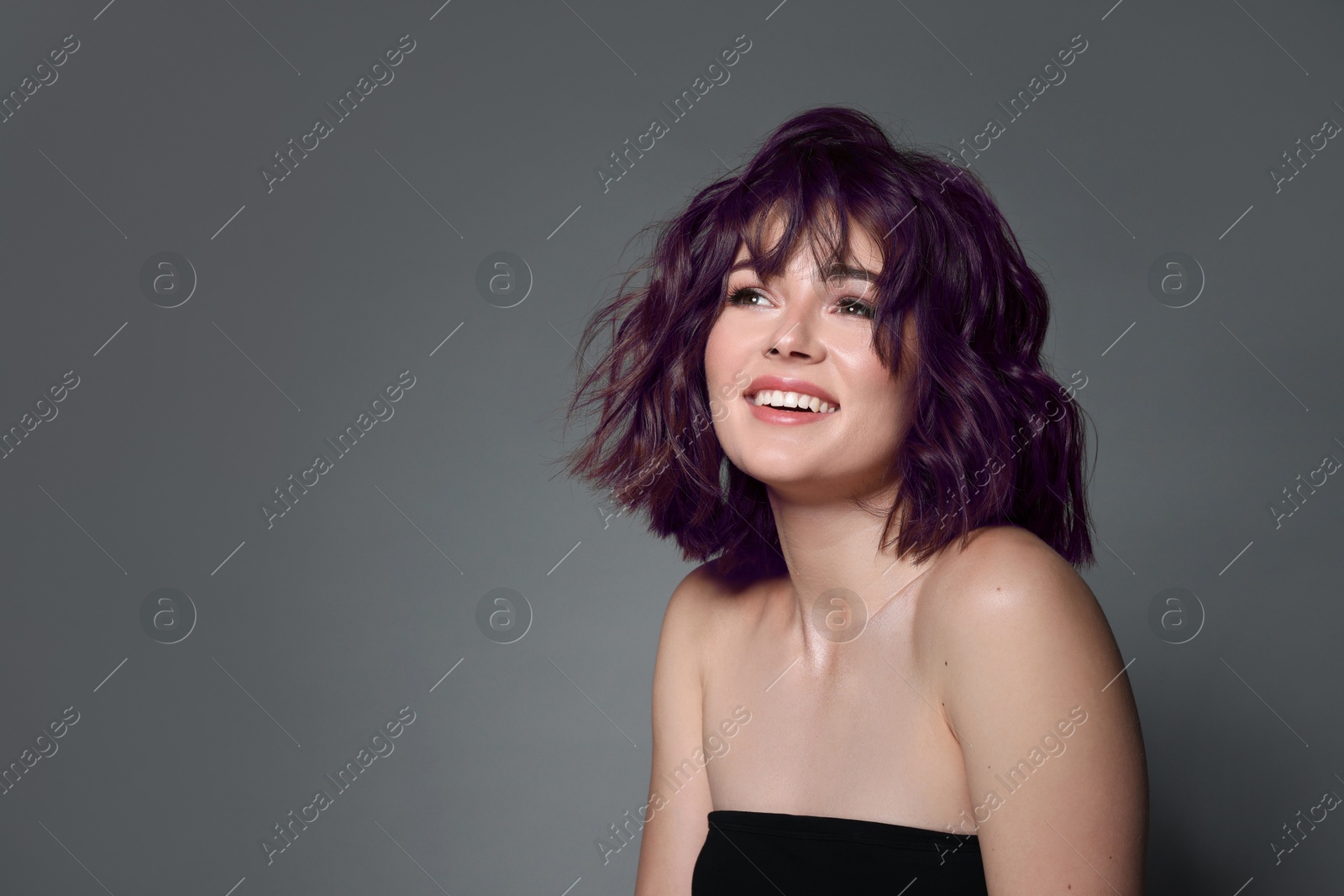 Image of Happy young woman with purple hair on grey background, space for text