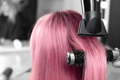 Hairdresser blow drying client's pink hair in salon, closeup