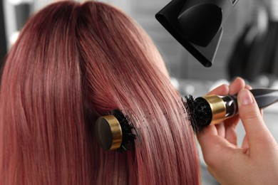 Hairdresser blow drying client's pink hair in salon, closeup