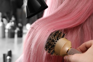 Hairdresser blow drying client's pink hair in salon, closeup