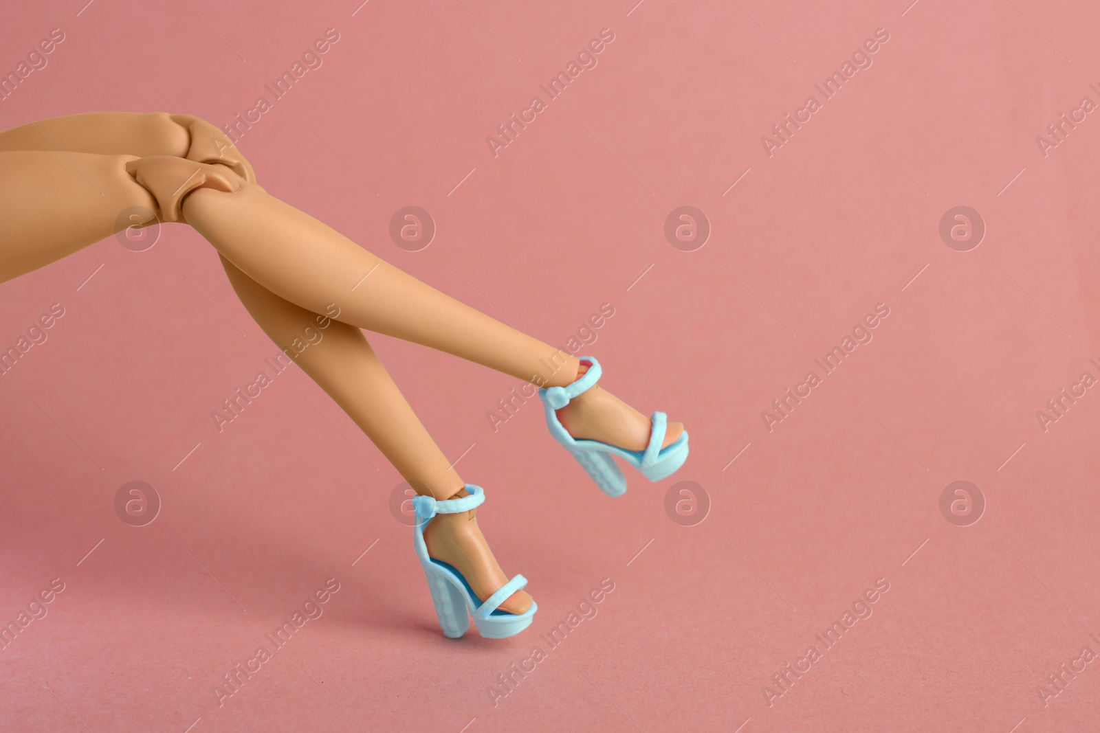 Image of Doll's legs with fancy shoes on coral background. Space for text