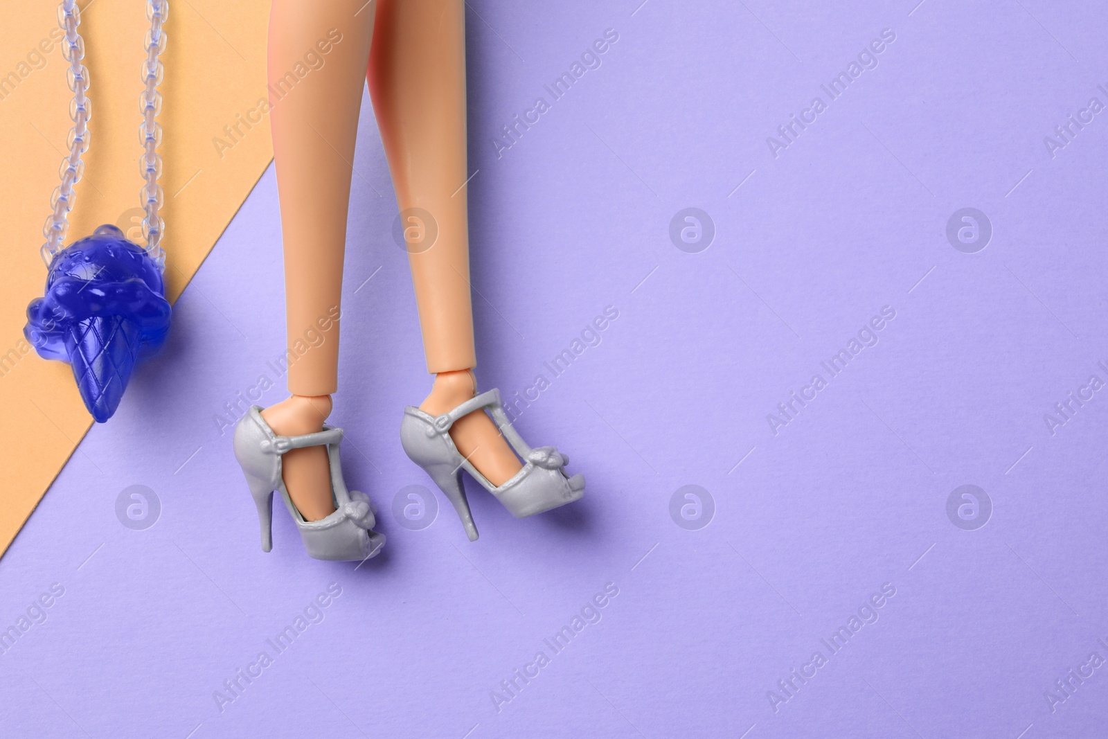 Image of Doll's legs with fancy shoes and bag in shape of ice cream on color background