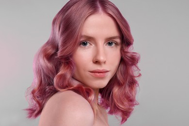 Pretty young woman with pink hair on light grey background