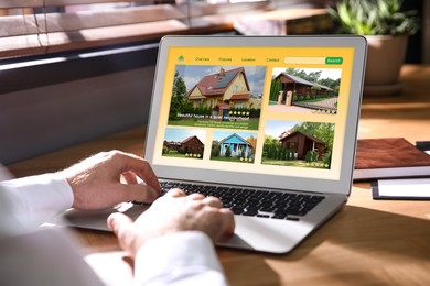 Man choosing dwelling on house hunting website via laptop at table, closeup