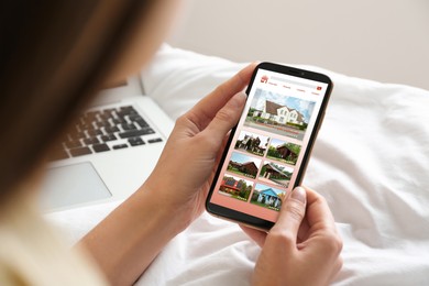 Woman choosing dwelling on house hunting website via smartphone at home, closeup