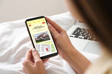 Woman choosing dwelling on house hunting website via smartphone at home, closeup