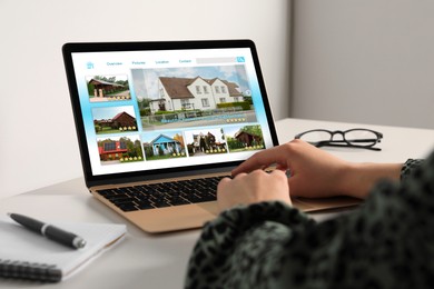 Woman choosing dwelling on house hunting website via laptop at table, closeup