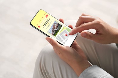 Woman choosing dwelling on house hunting website via smartphone indoors, closeup