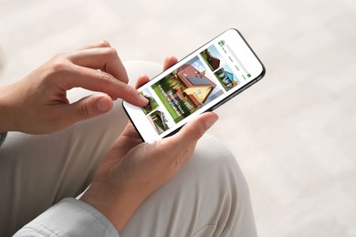 Image of Woman choosing dwelling on house hunting website via smartphone indoors, closeup