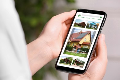 Woman choosing dwelling on house hunting website via smartphone, closeup