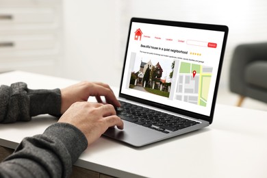 Man choosing dwelling on house hunting website via laptop at table, closeup