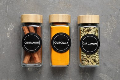 Image of Labelled jars with spices on grey table, flat lay. Cinnamon, curcuma and cardamom