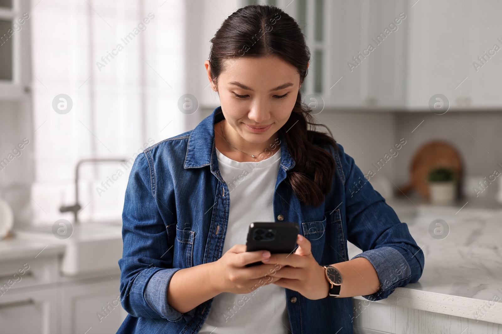 Photo of Beautiful young woman using smartphone in kitchen