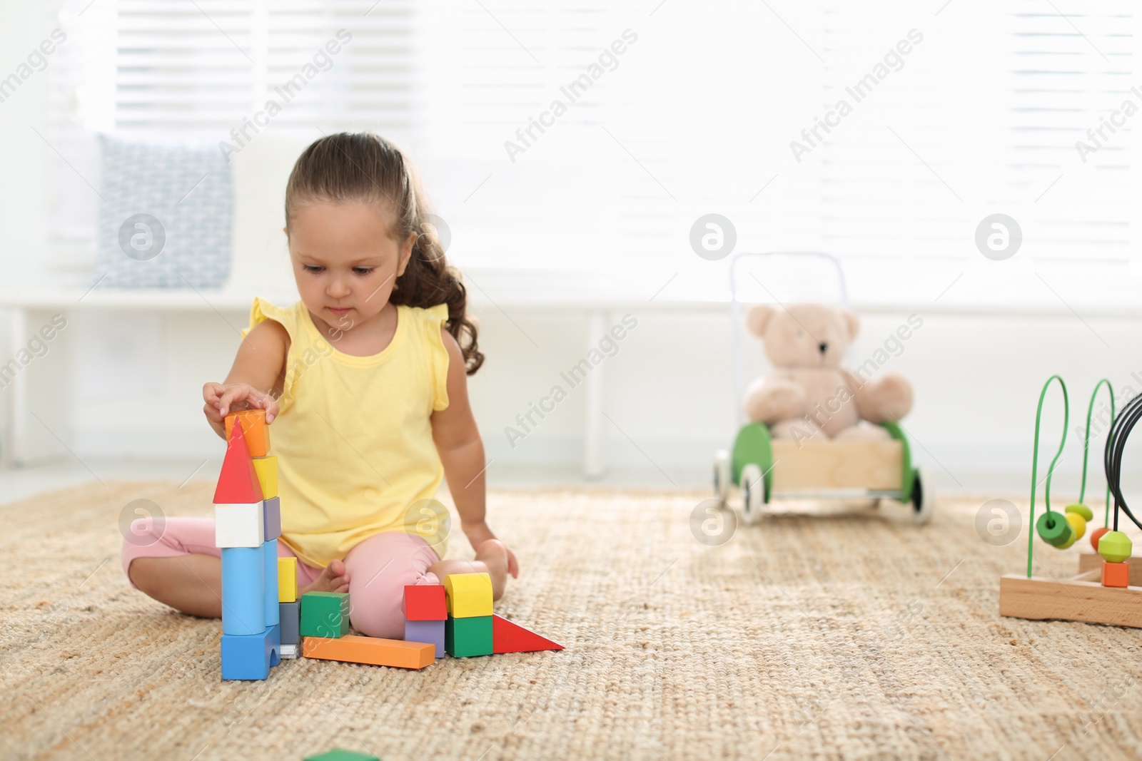 Photo of Cute little girl playing with colorful blocks on floor indoors, space for text. Educational toy