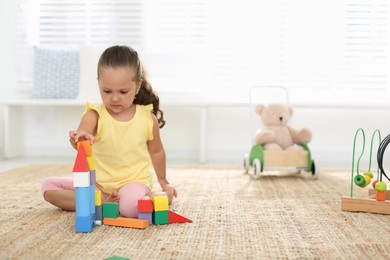 Photo of Cute little girl playing with colorful blocks on floor indoors, space for text. Educational toy