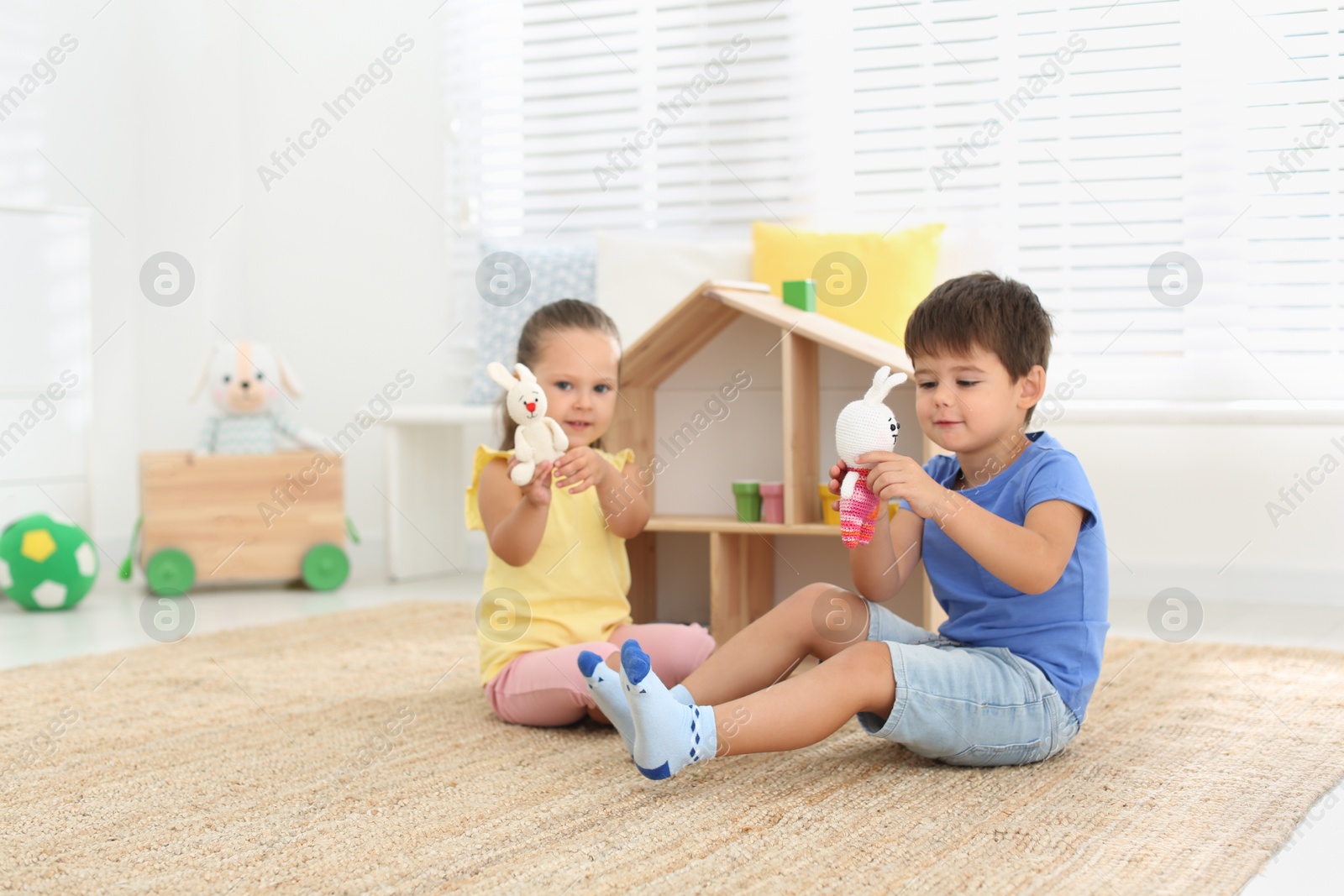 Photo of Cute little children playing with toys near wooden house on floor at home