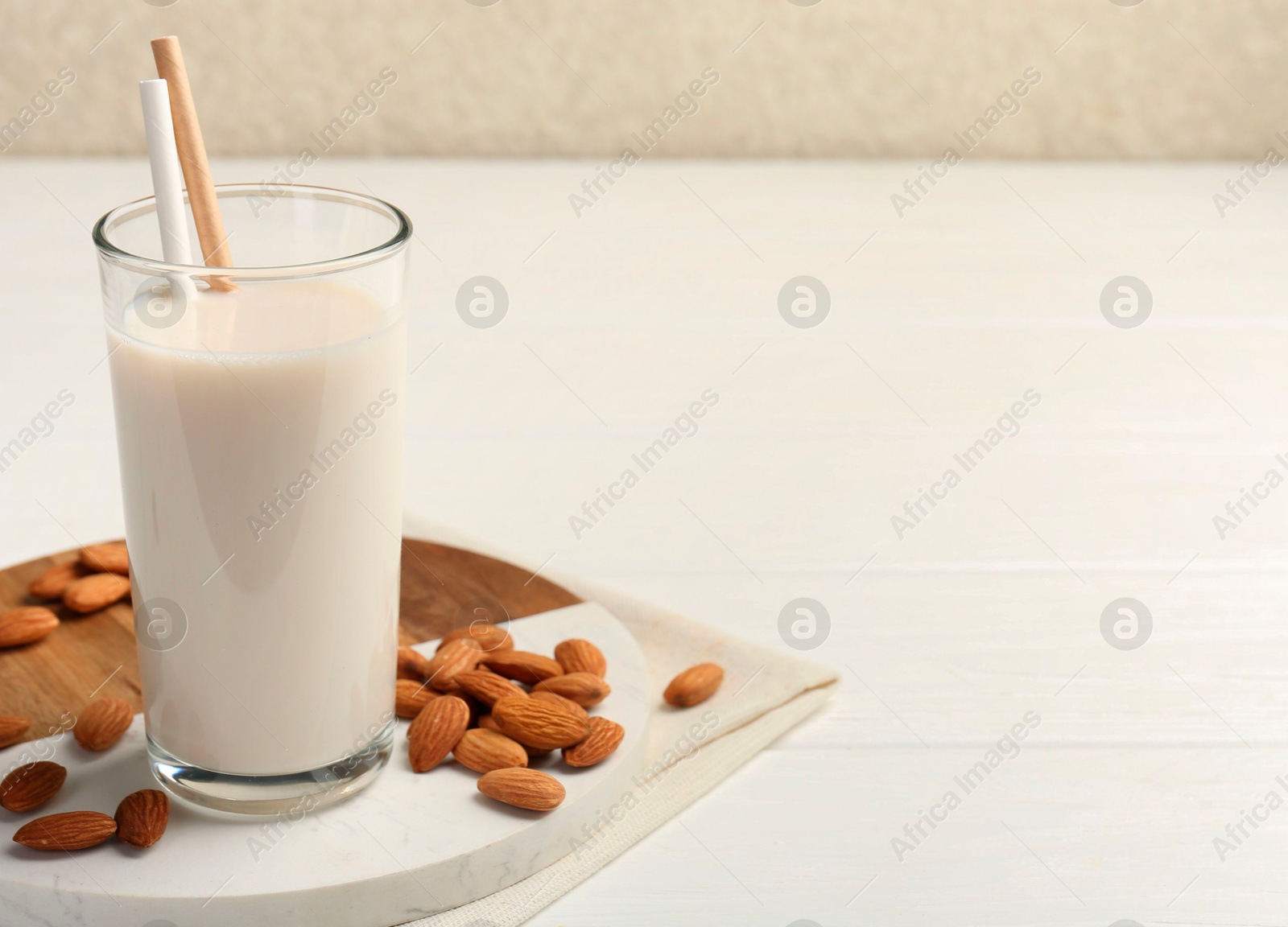 Photo of Glass of almond milk and almonds on white wooden table, space for text