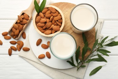 Photo of Glasses of almond milk, leaves and almonds on white wooden table, flat lay