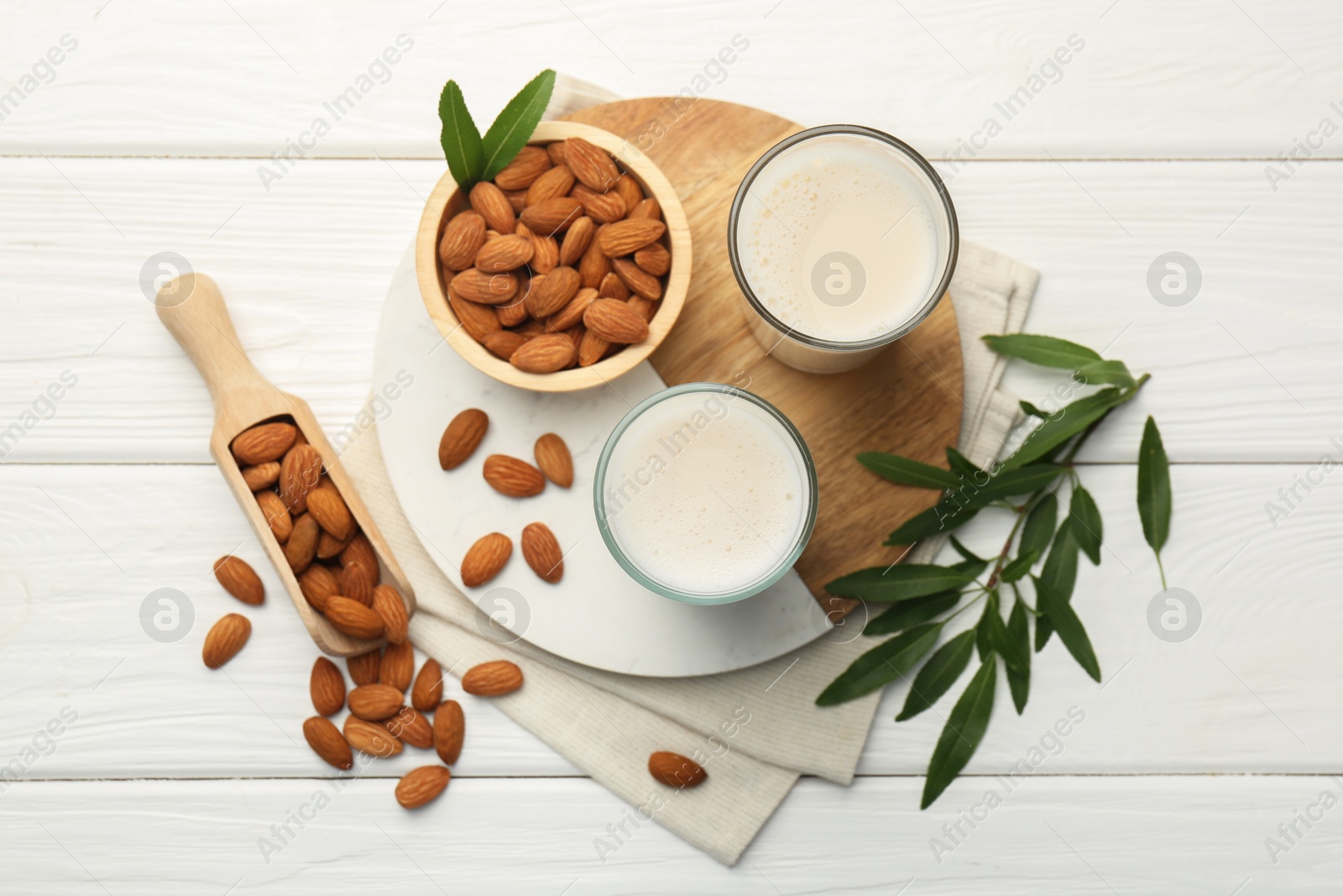 Photo of Glasses of almond milk, leaves and almonds on white wooden table, flat lay